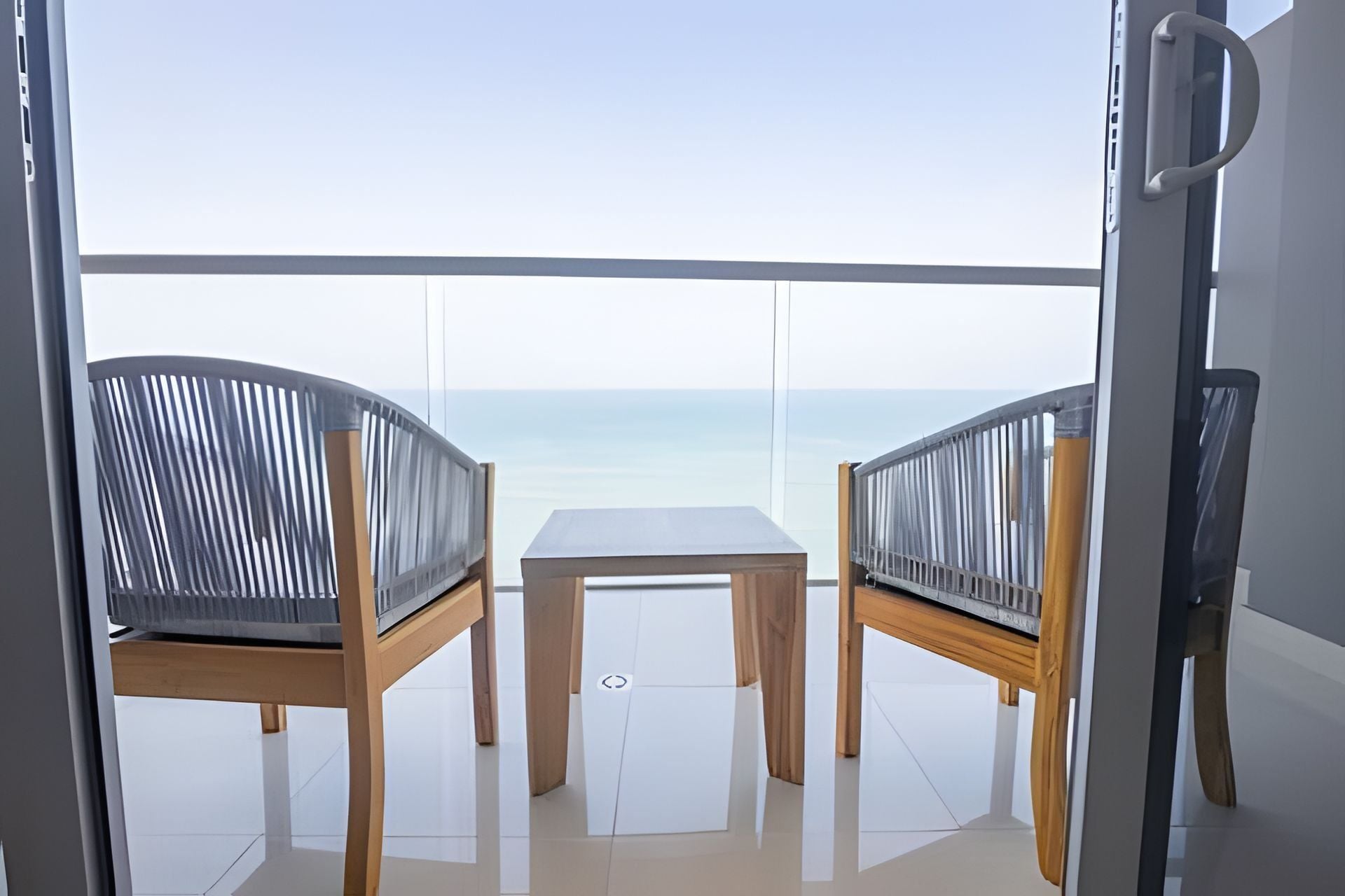Un balcón con dos sillas y una mesa, con vista despejada al mar.
