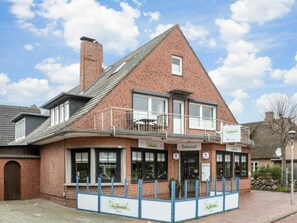 A brick building with a restaurant on the ground floor and a balcony with outdoor seating. - Holiday Apartment 1 (St. Peter-Ording)