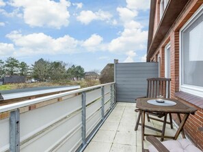 A balcony with a table and chair, a view of the sky, and a brick building in the background. - Holiday Apartment 1 (St. Peter-Ording)
