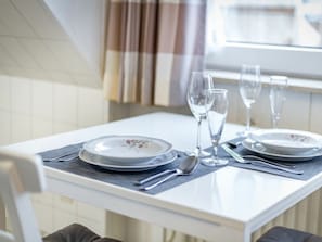 Une table à manger dressée avec des assiettes, des couverts et des verres à vin, avec une fenêtre et des rideaux visibles en arrière-plan.