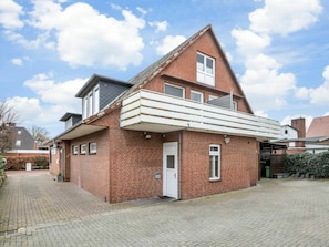 Une maison à deux étages, construite en briques, avec un balcon, une porte et un petit jardin.