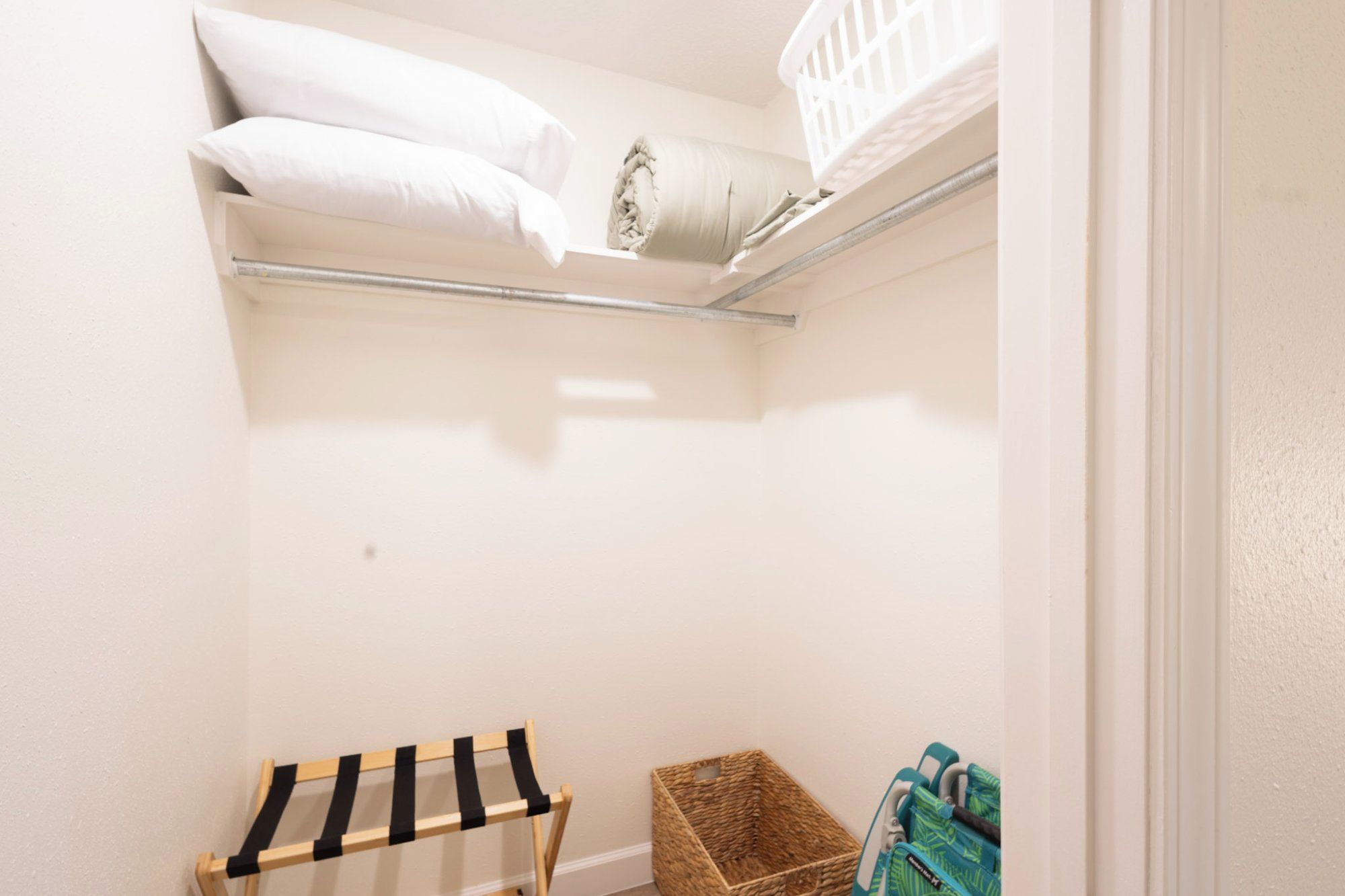A small storage closet with shelves, a hanging rack, and a wicker basket.