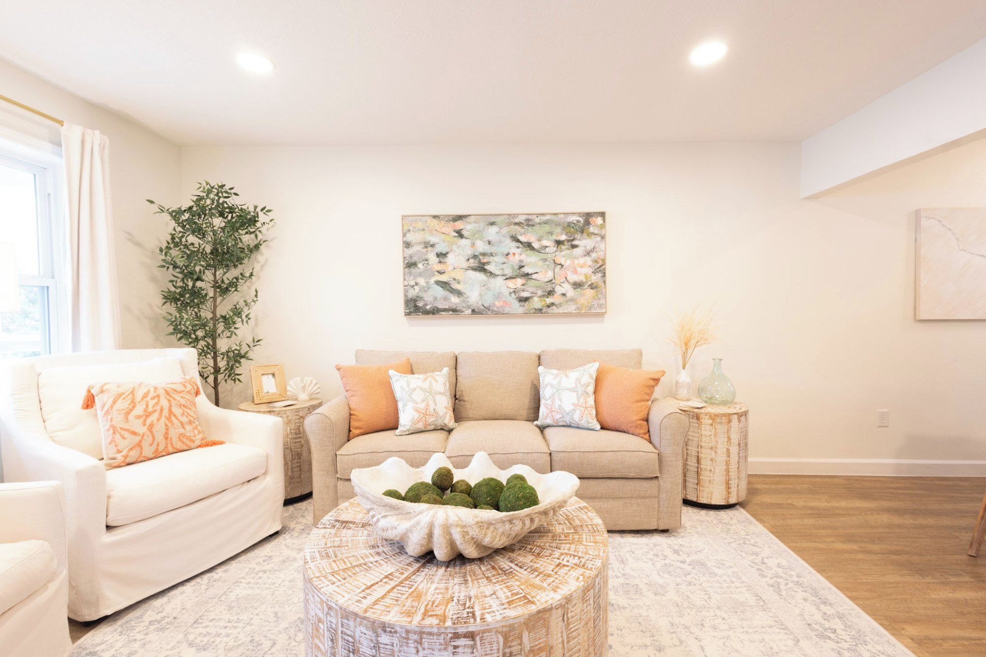 A living room with a beige sofa, white armchairs, a coffee table with decorative items, and a large abstract painting on the wall.