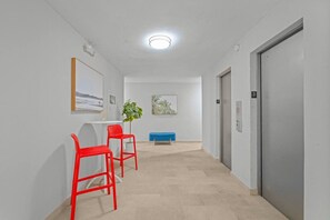 Ein Flur mit einem Schreibtisch, zwei roten Stühlen, einer blauen Bank und einer Tür mit der Nummer 3.