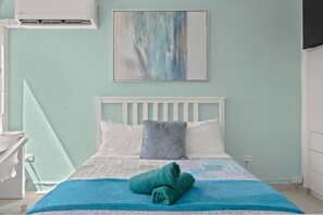 Ein Schlafzimmer mit einem Bett, Kissen, einer blauen Decke, einem Handtuch, einem weißen Kopfteil, einem Bild an der Wand und einer Klimaanlage.