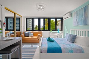 A modern bedroom with a bed, a sofa, a desk, and a window with a view of buildings and trees. - Casa Celeste | Sunlit Tropical Stay in Condado (San Juan)