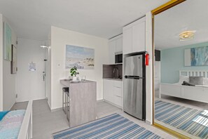 Eine moderne Küche mit einem Edelstahl-Kühlschrank, eine Essecke mit Barhocker und ein Schlafzimmer mit Bett und Nachttisch.