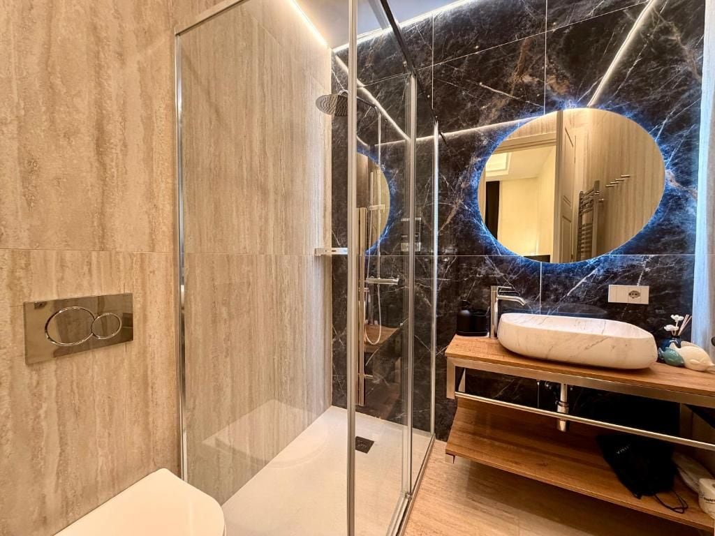 Un bagno moderno con cabina doccia in vetro, parete in marmo e mobile lavabo.