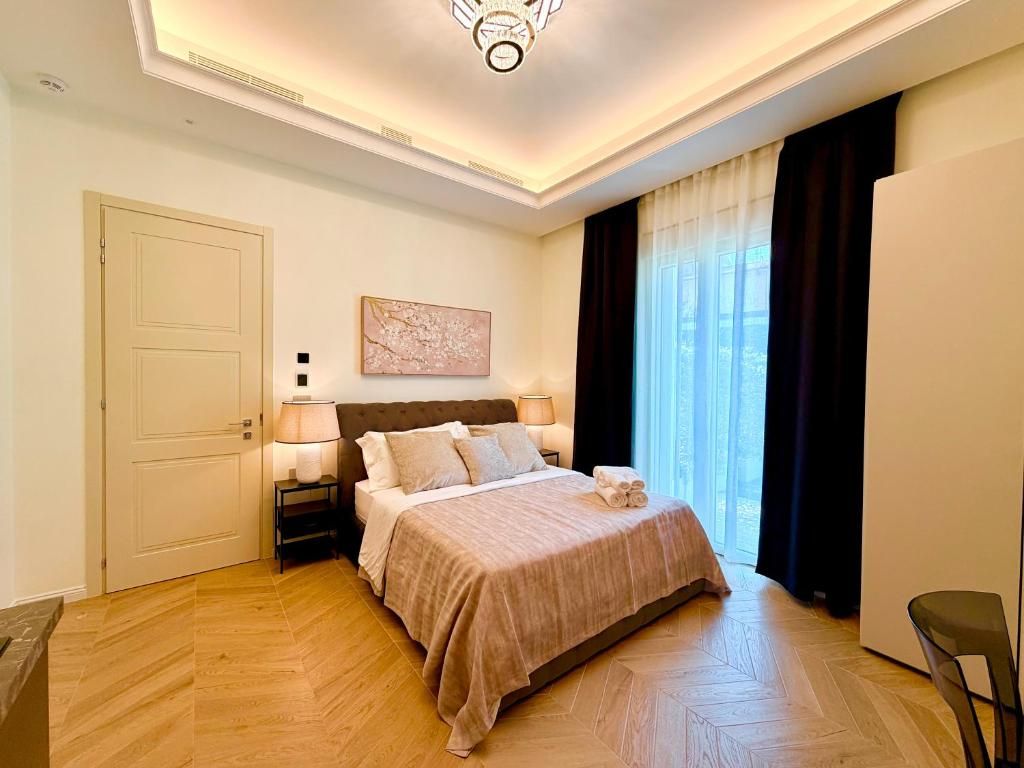 A hotel room with a bed, bedside lamps, a door, a window with curtains, and a chair.