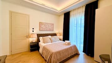 A hotel room with a bed, bedside lamps, a door, a window with curtains, and a chair.