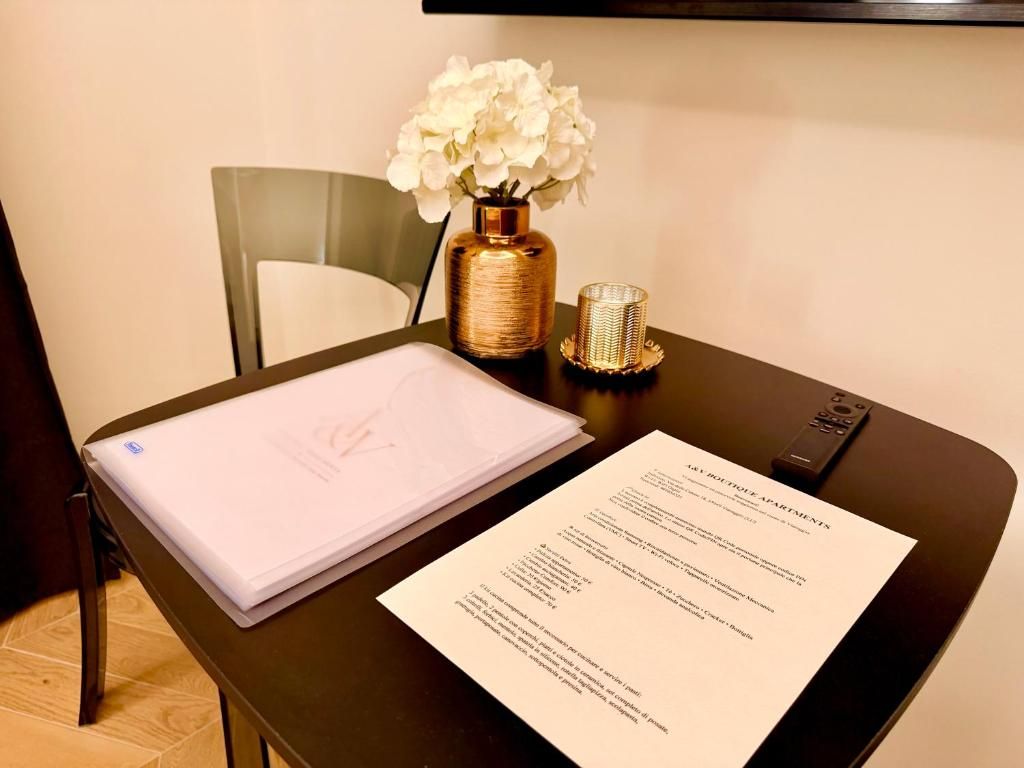 Una habitación de hotel con escritorio, laptop, un florero con flores y un menú.