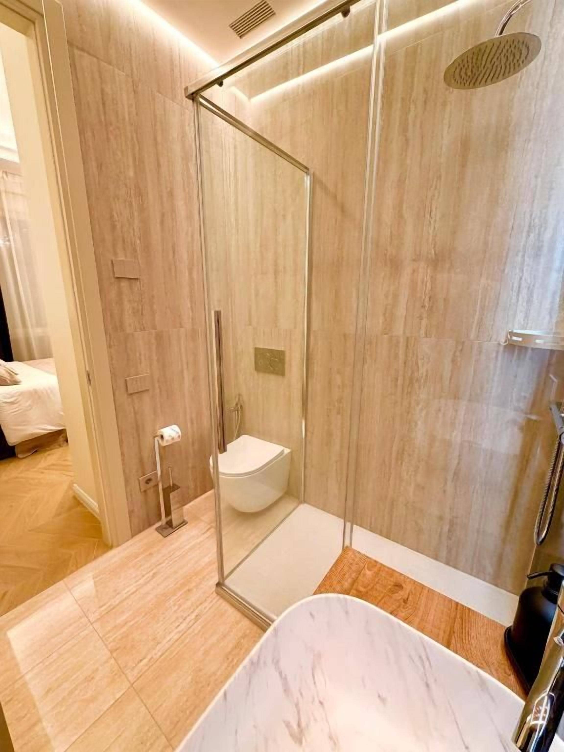 Un baño moderno con ducha envuelta en vidrio, inodoro blanco y bañera de mármol.