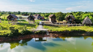 A rural setting with thatched-roof huts, a wooden dock, and a calm water body.