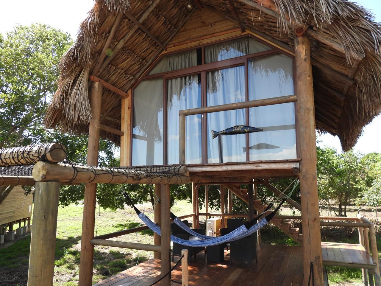 Una estructura de madera con techo de paja, una hamaca y una ventana con cortinas.