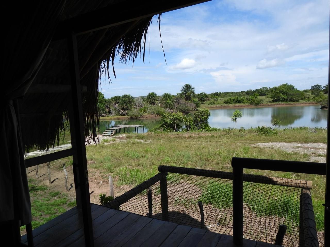 Una terraza de madera con techo de paja que da a un lago tranquilo y follaje circundante.