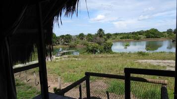 Una terraza de madera con techo de paja que da a un lago tranquilo y follaje circundante.