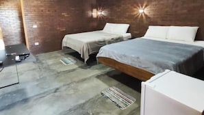 Un dormitorio con dos camas, una pared de ladrillo, un ventilador de techo y un pequeño armario blanco.
