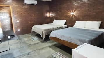 A bedroom with two beds, a brick wall, a ceiling fan, and a small white cabinet.