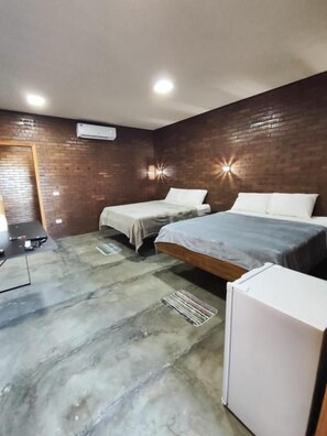 Une chambre avec deux lits, un mur en briques, un ventilateur de plafond et une petite armoire blanche.
