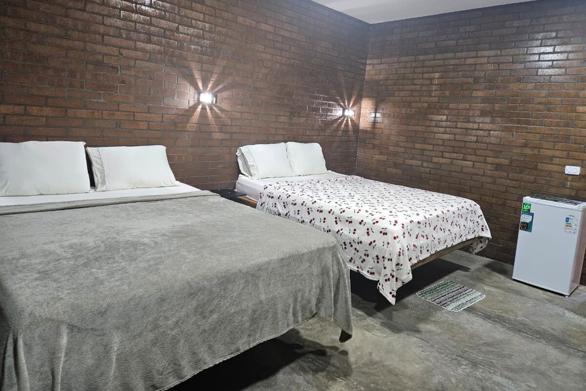 Una habitación con dos camas, una pared de ladrillo y un refrigerador.
