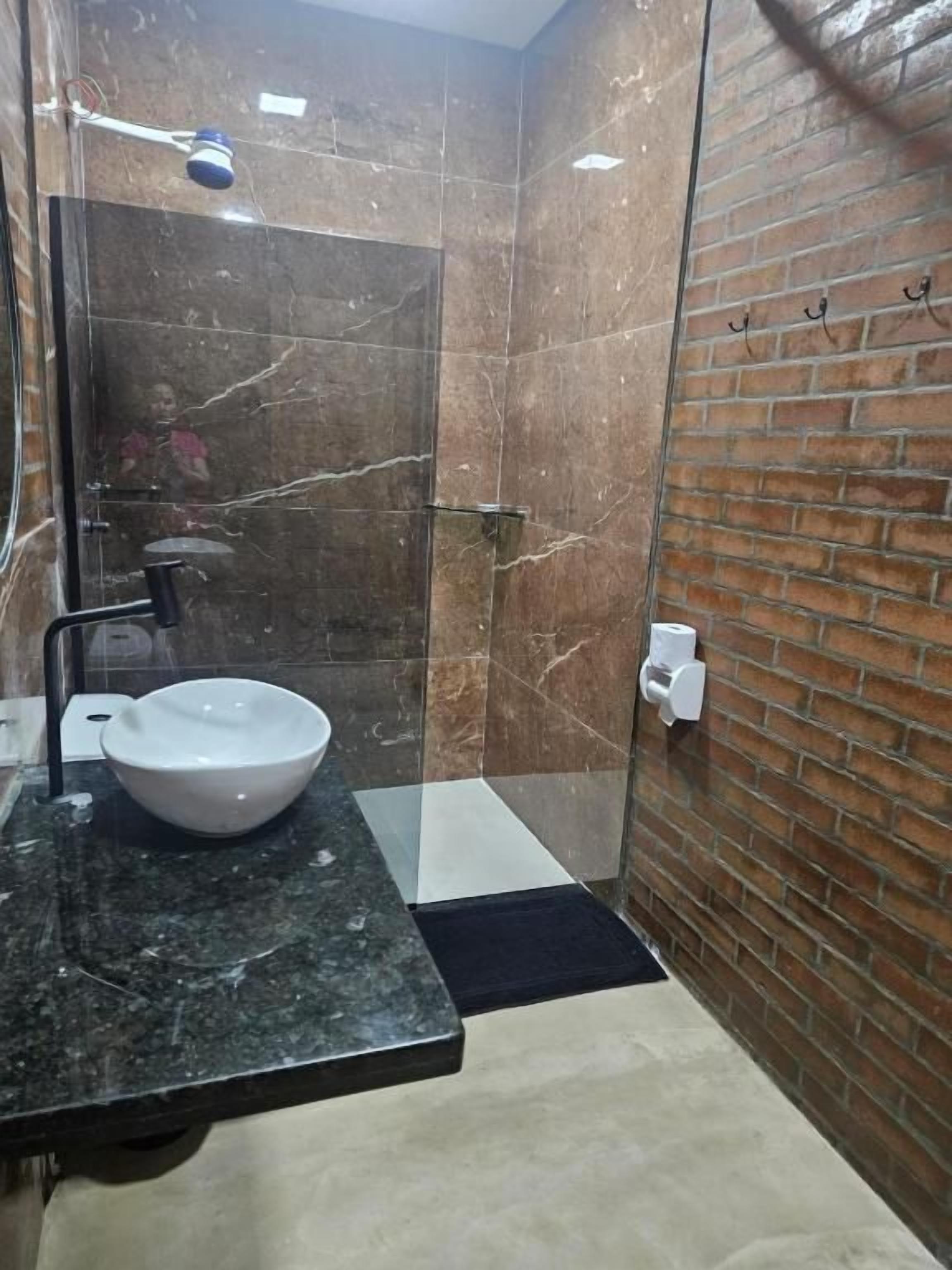 Un baño moderno con ducha envuelta en vidrio, lavamanos de mármol y pared de ladrillo.