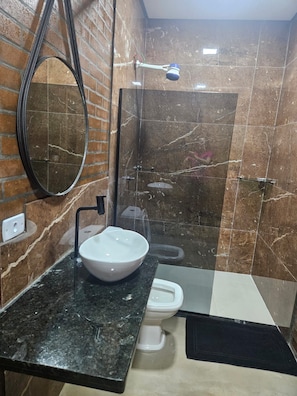 Un baño con pared de mármol, lavamanos blanco, inodoro y zona de ducha.