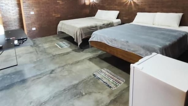 Un dormitorio con dos camas, una pared de ladrillo y un aire acondicionado instalado en el techo.