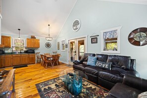 A spacious living room with a leather sofa, wooden dining table, and a kitchen in the background. - Gorge-Us Getaway: A Cozy Retreat for Family and Friends (Zoe)