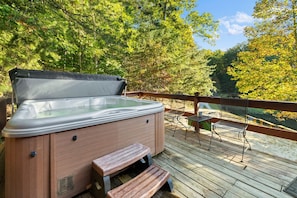 Ein Whirlpool auf einer Holzterrasse mit einer Bank und Stühlen, umgeben von Bäumen.