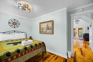 Ein Schlafzimmer mit einem Bett, einem Gemälde, einer Kompass-Wanddekoration und Blick in einen anderen Raum.