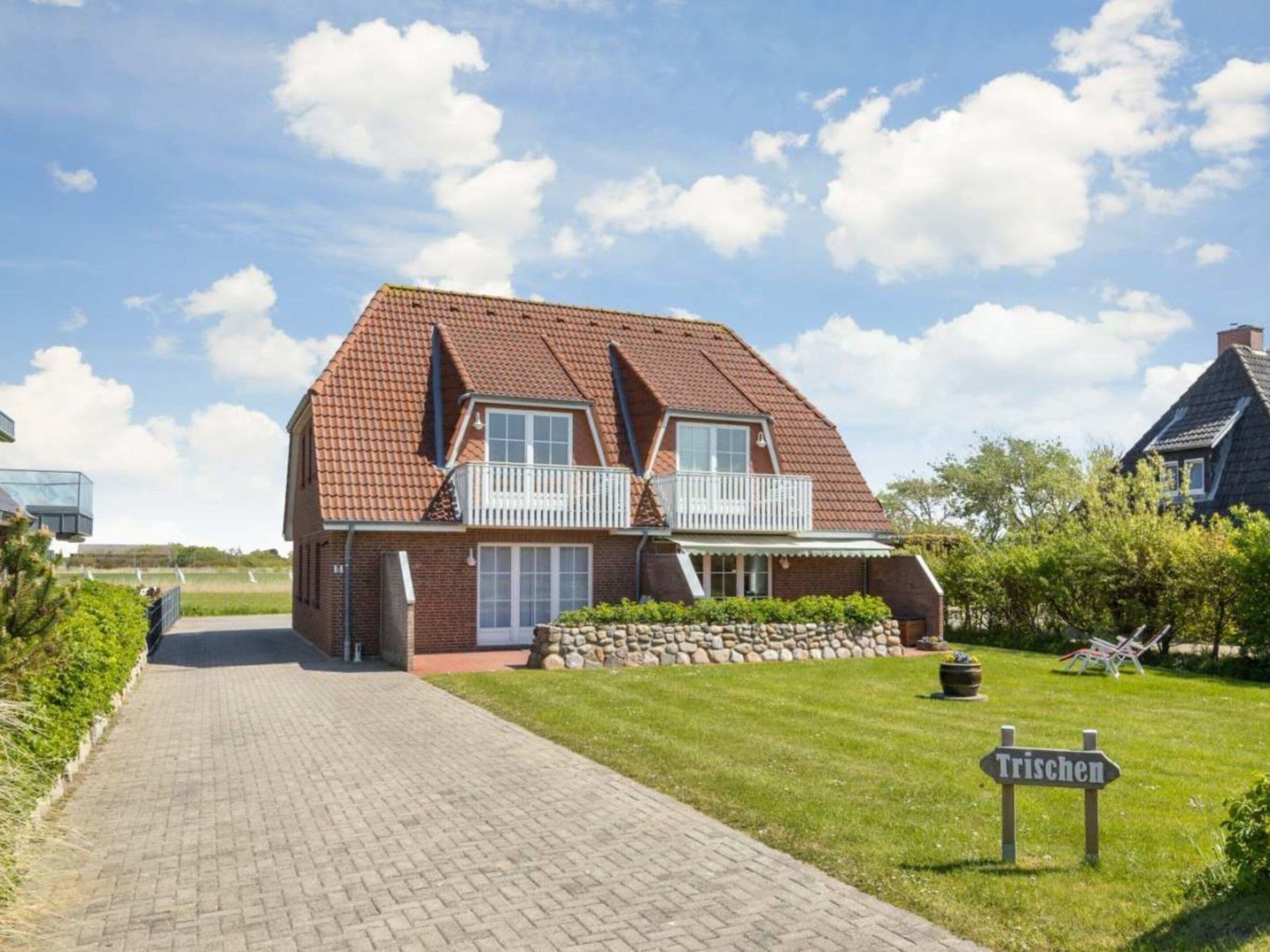 Een huis met twee verdiepingen, een schuin dak, een balkon en een verharde oprit naar de ingang.
