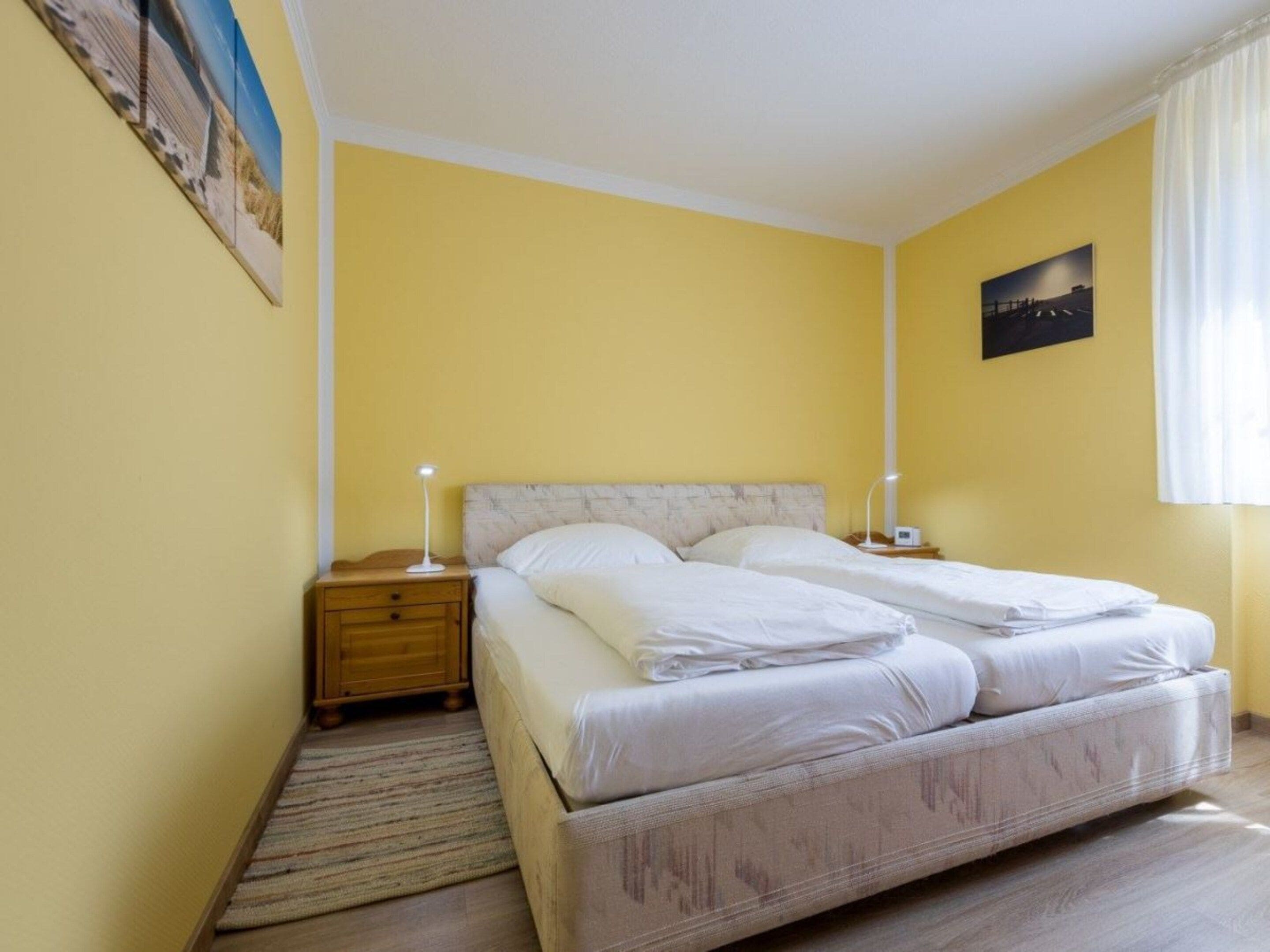 Un lit double avec du linge de lit blanc, une table de chevet avec une lampe et un tableau au mur.