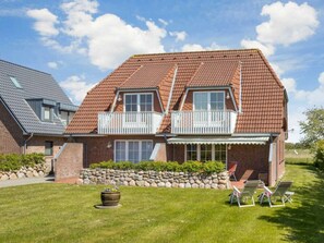 A two-story house with a tiled roof, a balcony, and a stone wall in the front yard. - 1 in the House "trischen" (St. Peter-Ording)