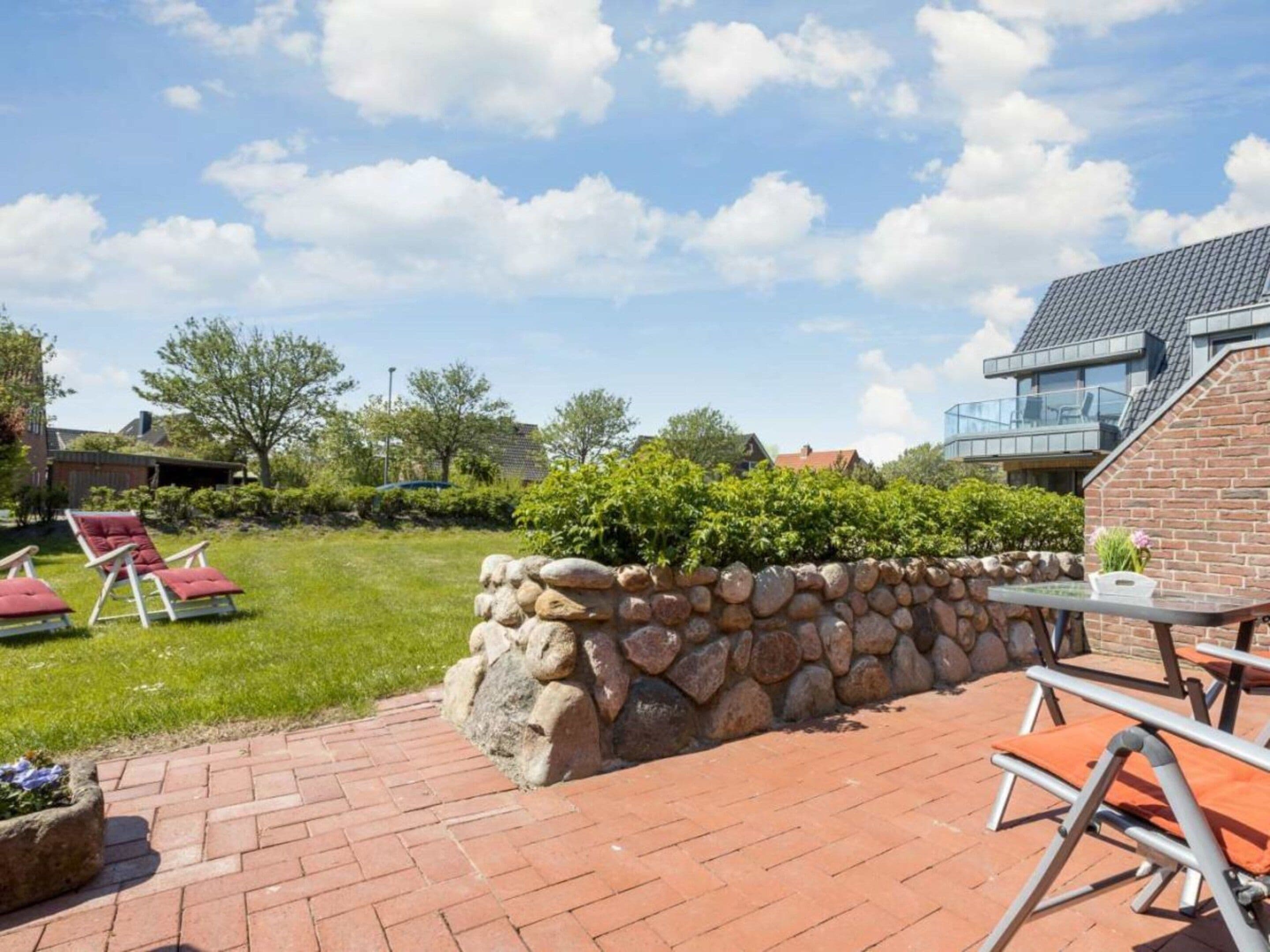 Eine Terrasse mit Steinmauern, Gartenmöbeln und Blick auf ein modernes Gebäude.