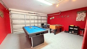 A room with a pool table, a foosball table, and a garage door. - 4 BD/ 3 BA/ Rolling Hills Estates (7952 HE) (Kissimmee)