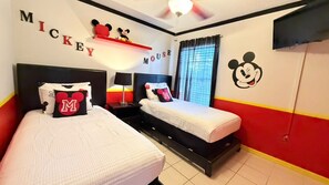 Ein Schlafzimmer mit zwei Betten, Mickey Mouse Dekoration und einer rot-gelb gestreiften Wand.