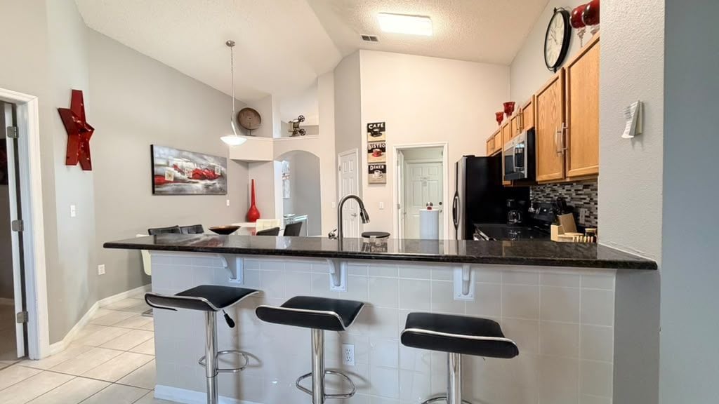 A modern kitchen with a central island, bar stools, and a dining area.