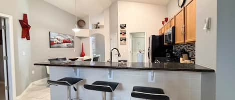A modern kitchen with a central island, bar stools, and a dining area.