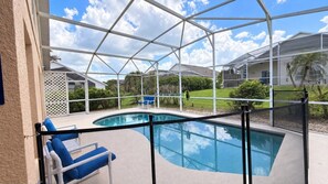 Ein überdachter Pool mit Glasveranda, blauen Liegestühlen und Blick auf eine Wohngegend.