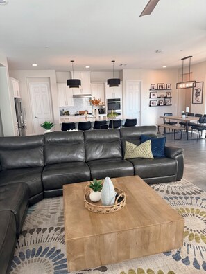 A modern living room with a leather sectional sofa, a wooden coffee table, and a dining area with a wooden table and chairs. - Relax, unwind and enjoy Lake Las Vegas! 
6 month bookings only (Henderson)