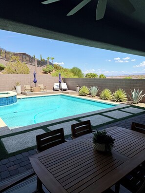 Una piscina con sillones de descanso y una mesa, rodeada de un muro de ladrillo y vegetación.