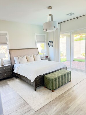 A bedroom with a large bed, bedside tables, a green ottoman, and a view through a sliding glass door. - Relax, unwind and enjoy Lake Las Vegas! 
6 month bookings only (Henderson)