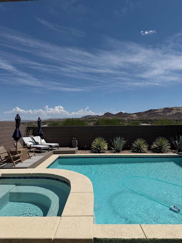 Una piscina con sillas de descanso y sombrillas, rodeada de jardines con plantas desérticas y vistas a montañas distantes.