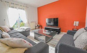 A living room with a sofa set, a coffee table, a flat-screen TV, and a bright orange accent wall. - The House of Viennes (SAINT ANDRE LES VERGERS)