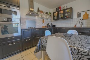 A modern kitchen with built-in ovens, a dining table with chairs, and a wine rack on the wall. - The House of Viennes (SAINT ANDRE LES VERGERS)