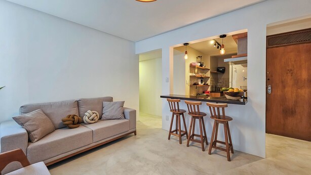 Uma sala de estar moderna com um sofá, uma mesa de centro e um espaço bar com banquetas.