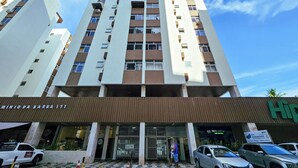 Edifício com vários andares e design arquitetônico moderno, destacando uma entrada imponente com portão de metal e piso padronizado.