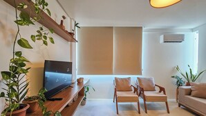Uma sala de estar moderna com televisão de tela plana, duas poltronas, um sofá e plantas em vasos.