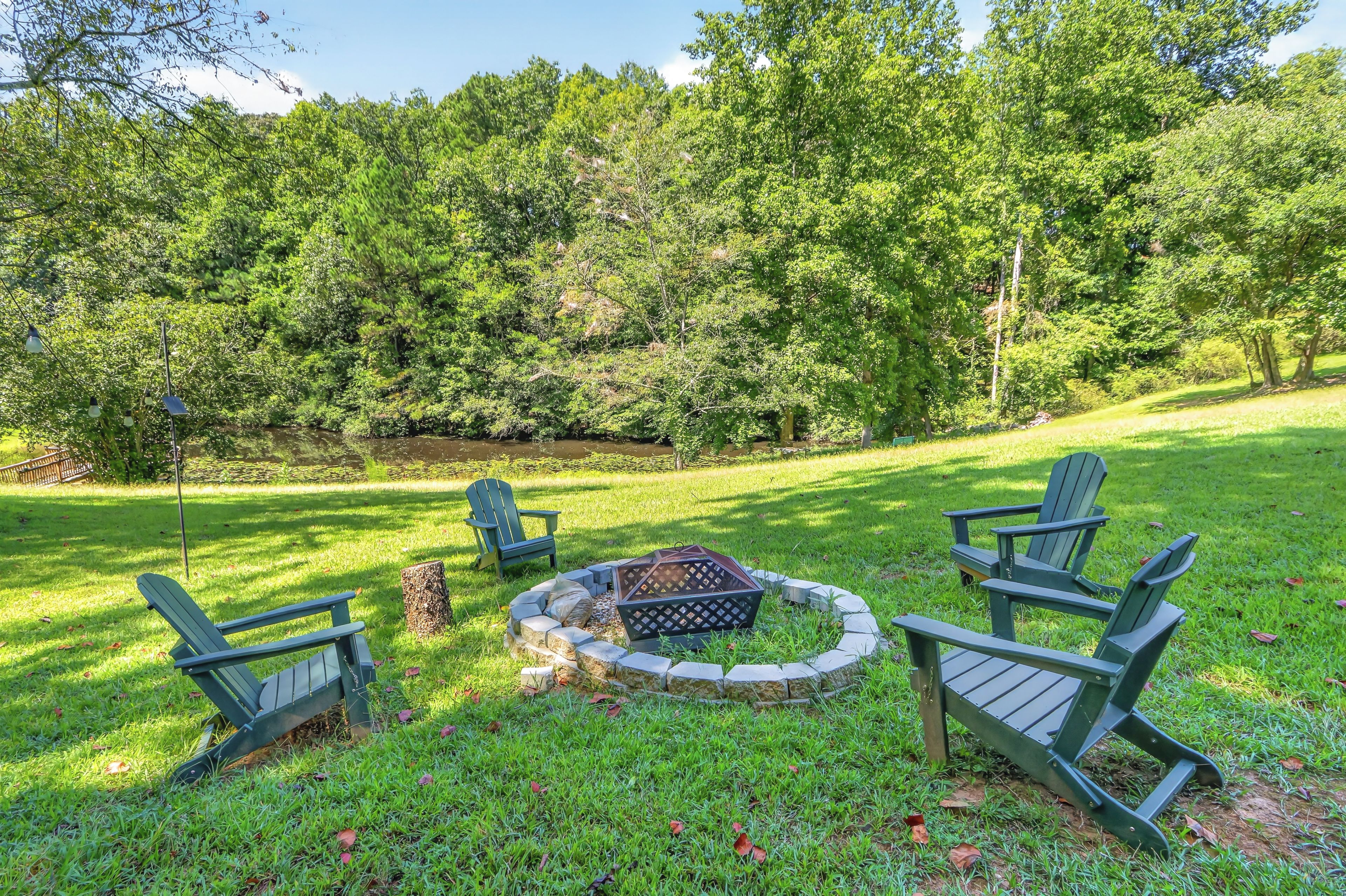 A grassy outdoor area with a fire pit and Adirondack chairs.