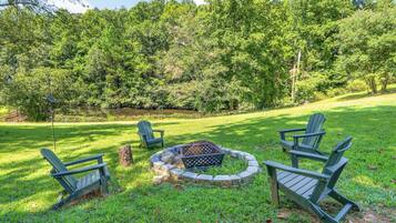 A grassy outdoor area with a fire pit and Adirondack chairs.